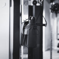 Black leather bag hanging on a metal hook against a neutral background